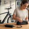 Mujer conectando el cable de carga a una batería de bicicleta eléctrica moderna de PuntoElectric sobre un banco de trabajo en un taller.