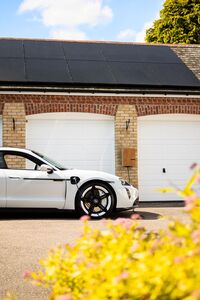 Coche eléctrico blanco aparcado frente a un garaje con paneles solares, representando la tecnología V2G y carga bidireccional.