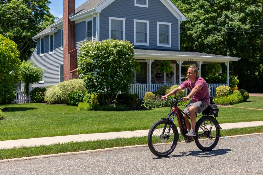 Hombre paseando en bicicleta eléctrica por una zona residencial con la batería integrada visible en el cuadro