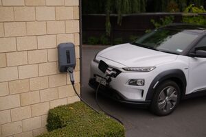 Coche eléctrico blanco conectado a un punto de recarga de pared en el exterior de una vivienda.