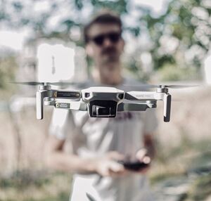 Primer plano de un dron ligero en vuelo mientras un piloto lo maneja al fondo al aire libre.